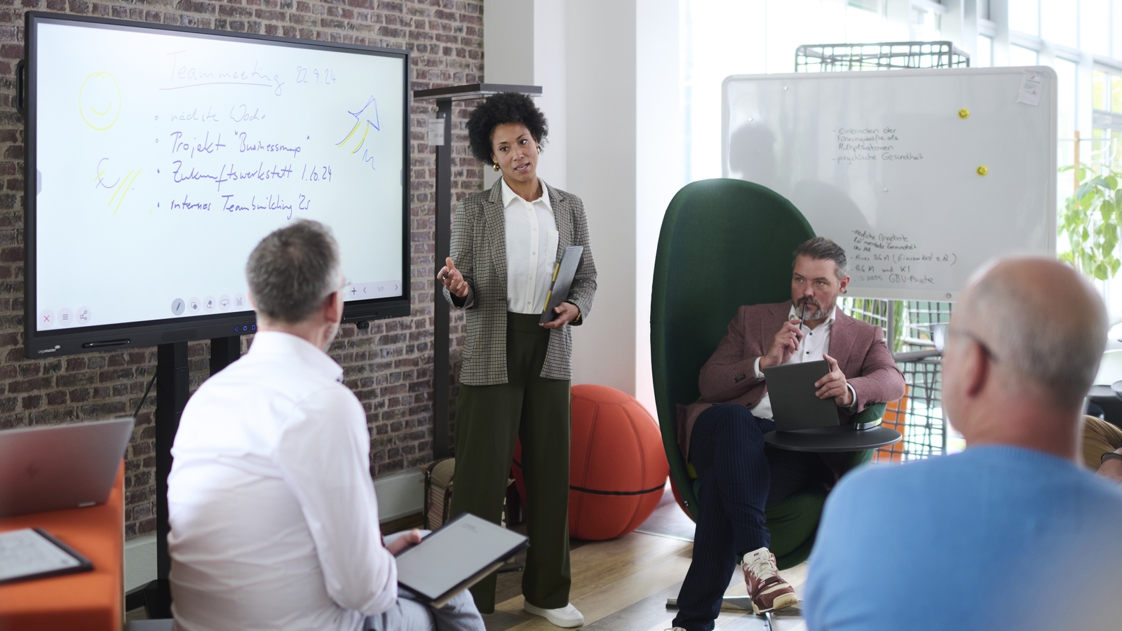 "Johanna steht in einem Seminar vor einer Gruppe von Menschen. Reflexionsphase der sichtbar gemachten Teamdynamik"
