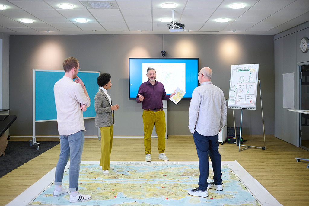 "Ein Team steht auf der Bodenkarte des menschlichen Verhaltens in einem MapsTell
                Workshop"